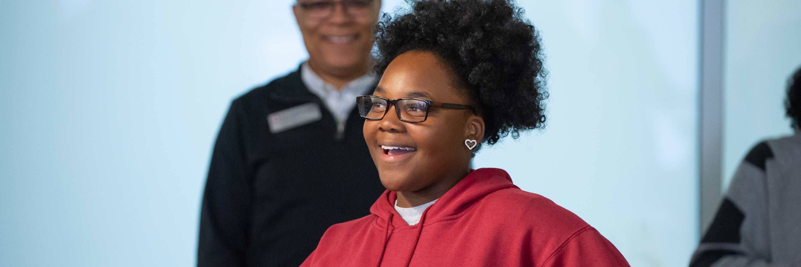 一个微笑的学生，老师在她身后看着她。