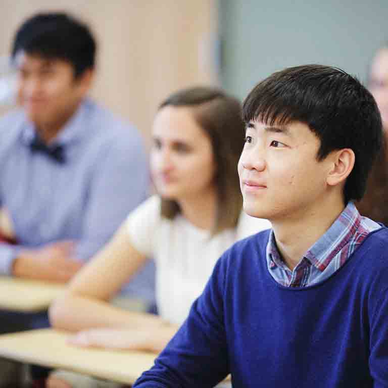 一个男同学坐在讲堂聚精会神地看向前面。