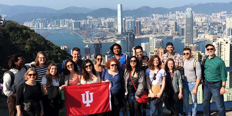 一群学生在旅行中举着国际大学的旗帜，背景是香港的城市景观。