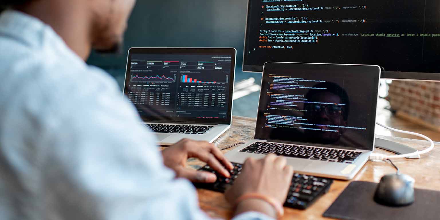 一个人与另一个笔记本电脑和一台笔记本电脑上写代码桌面监控坐在他的办公桌。